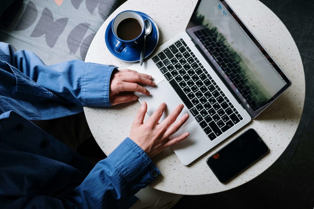 man in Blue Denim Jeans Using Macbook Pro Beside White Ceramic Mug on White Table