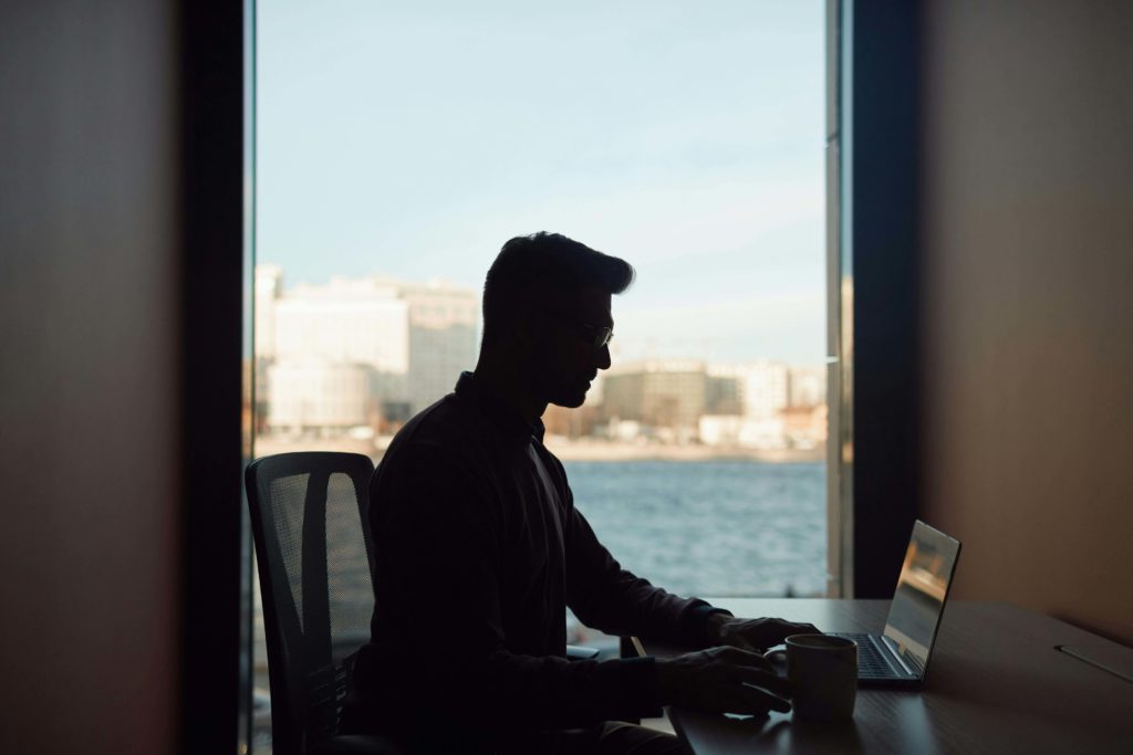 Silhouette of a Man Using a Laptop while Sitting