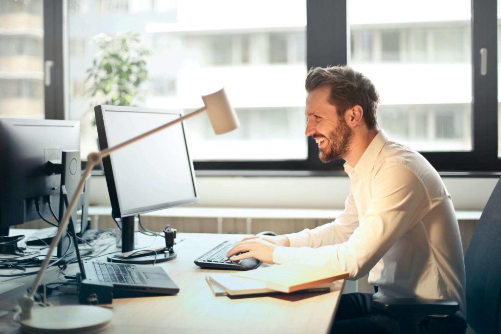 A Man Facing Black Computer Set and Smiling