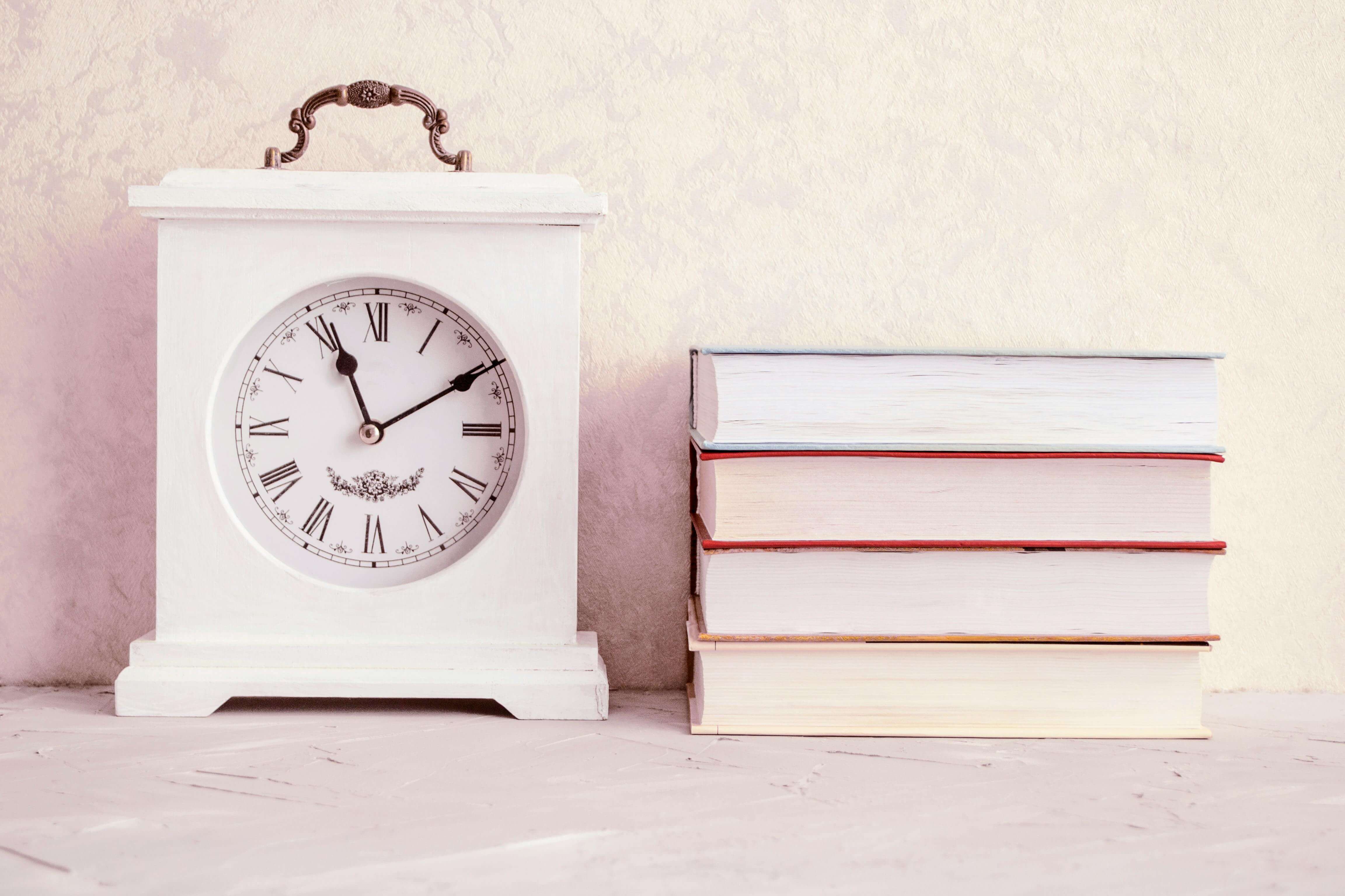 Photograph of a White Vintage Clock Beside a Stack of Books