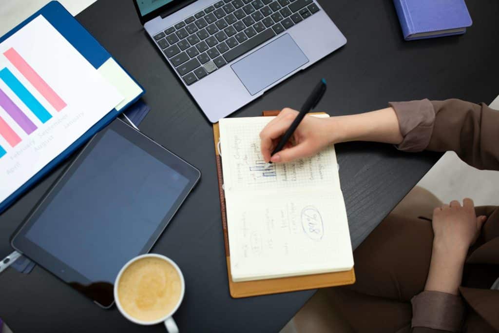 A Person Writing on the Notebook on the Work Desk